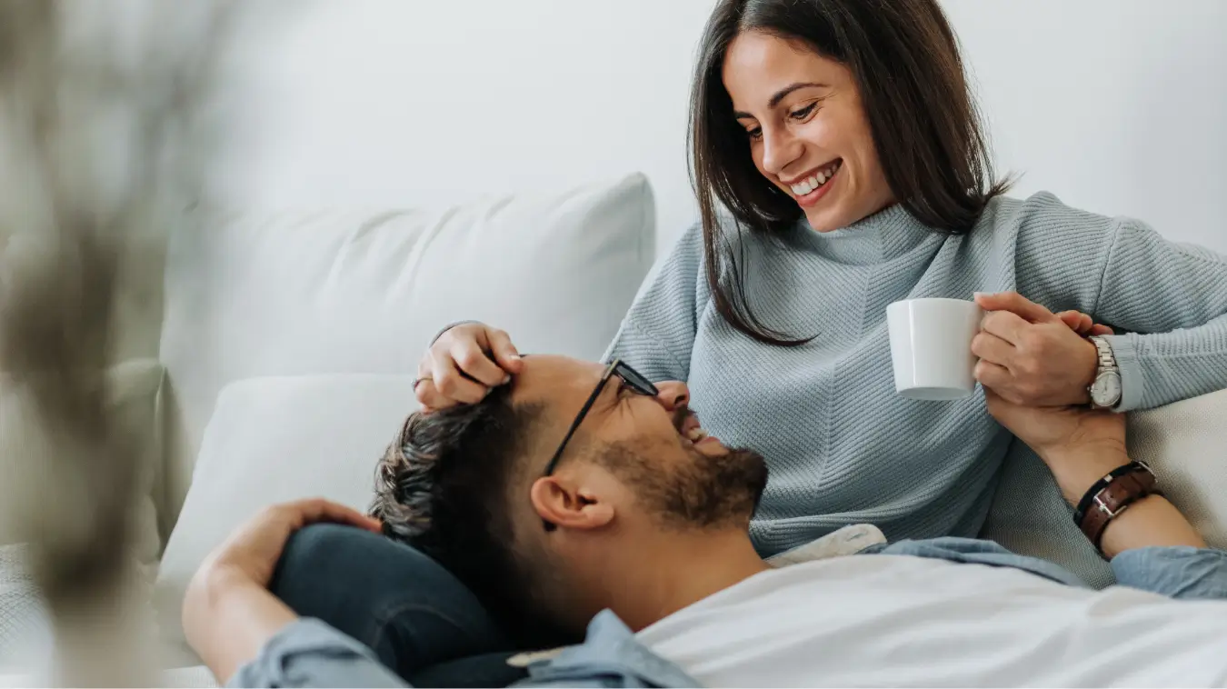 Ein lächelndes Paar entspannt auf einer Couch, die Frau hält eine Tasse.