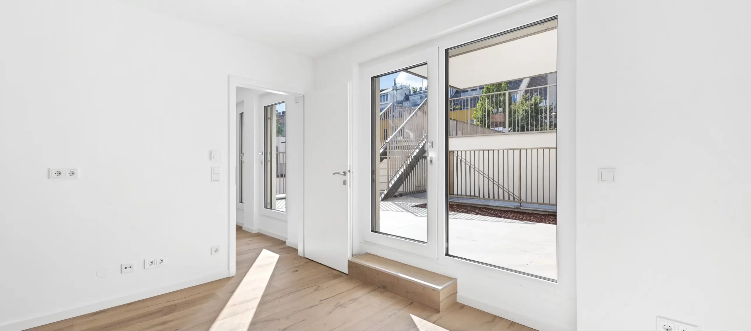 Heller Raum mit Holzboden und Tür zu einem Innenhof mit Treppe.
