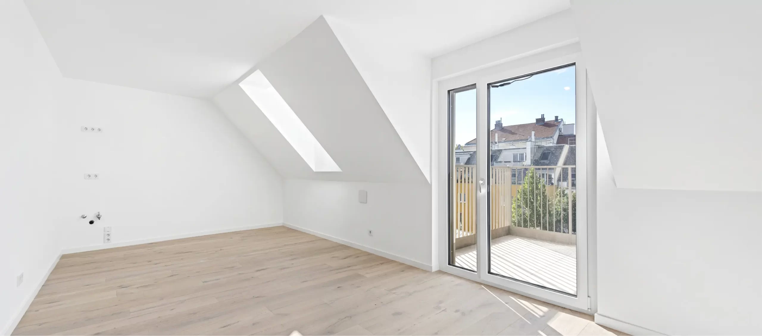 Dachzimmer mit Holzboden, Dachfenstern und einer Glasschiebetür zu einem Balkon.